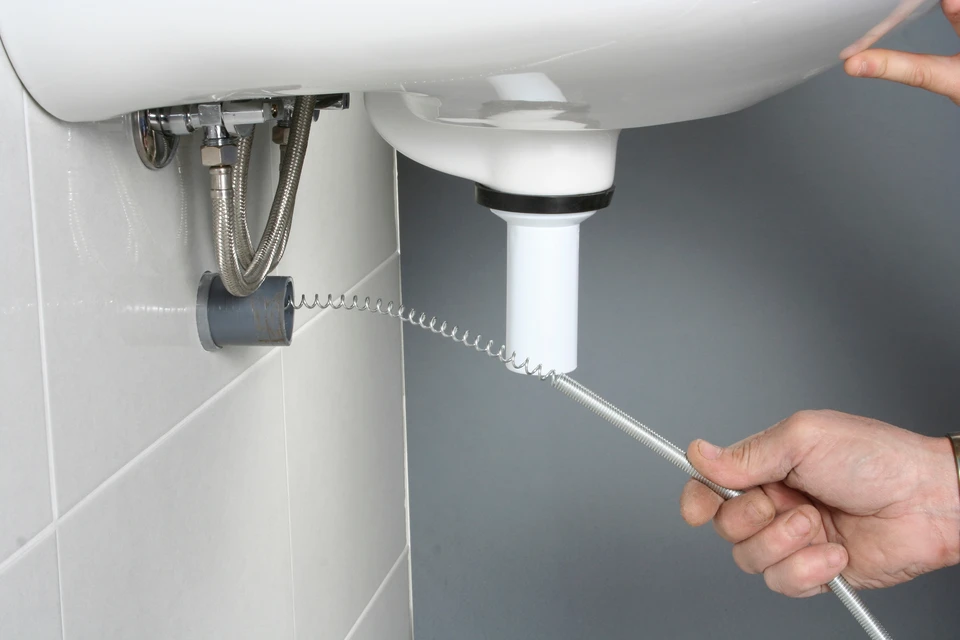 Technicien en combinaison rouge effectue débouchage canalisation dans toilettes résidentielles avec furet électrique professionnel