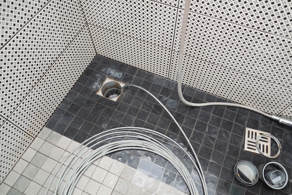 Un plombier en combinaison rouge effectue un débouchage de canalisation dans des toilettes blanches à l'aide d'un furet électrique