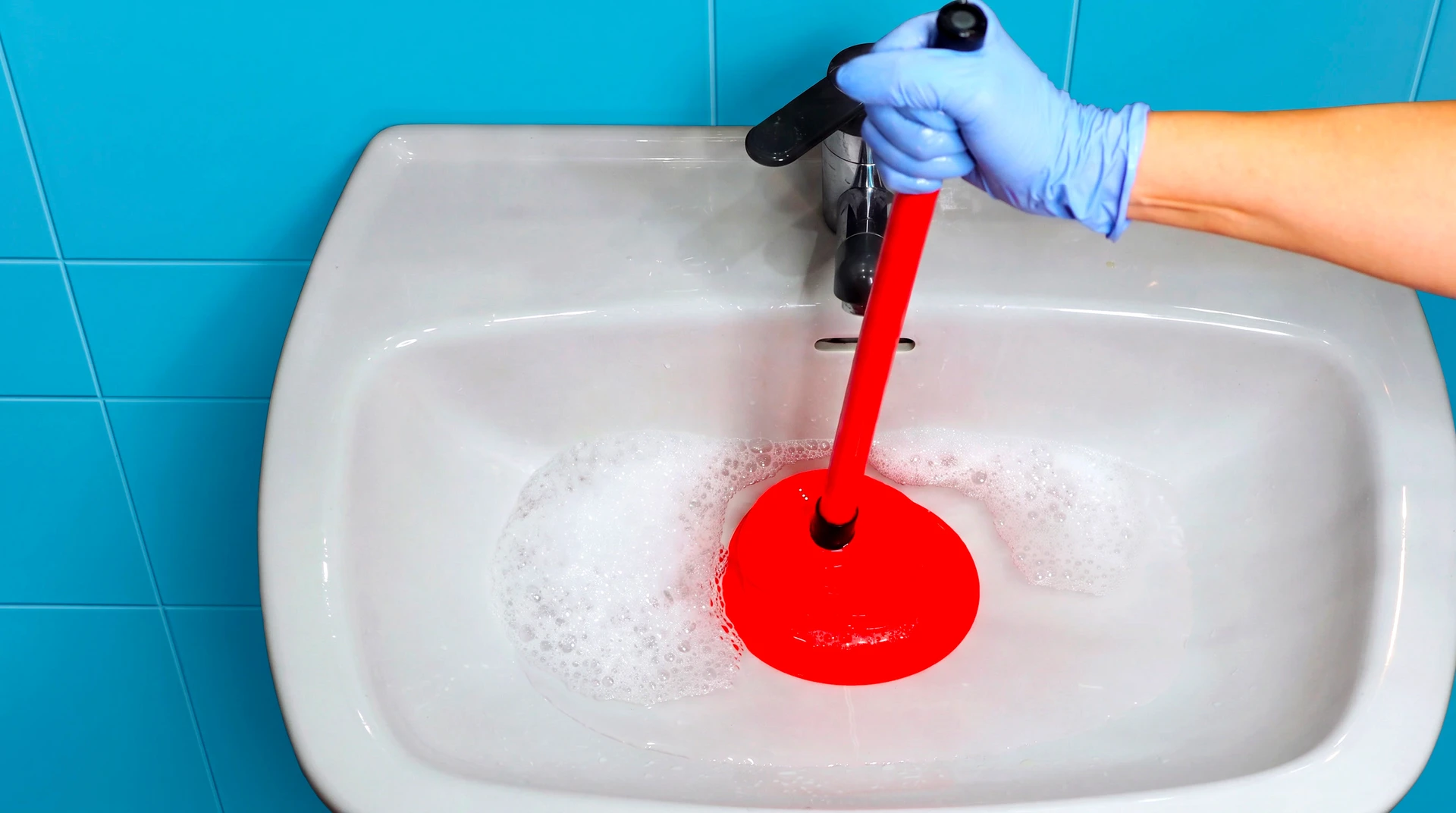 Un plombier en combinaison rouge effectue un débouchage de canalisation dans des toilettes blanches à l'aide d'un furet électrique